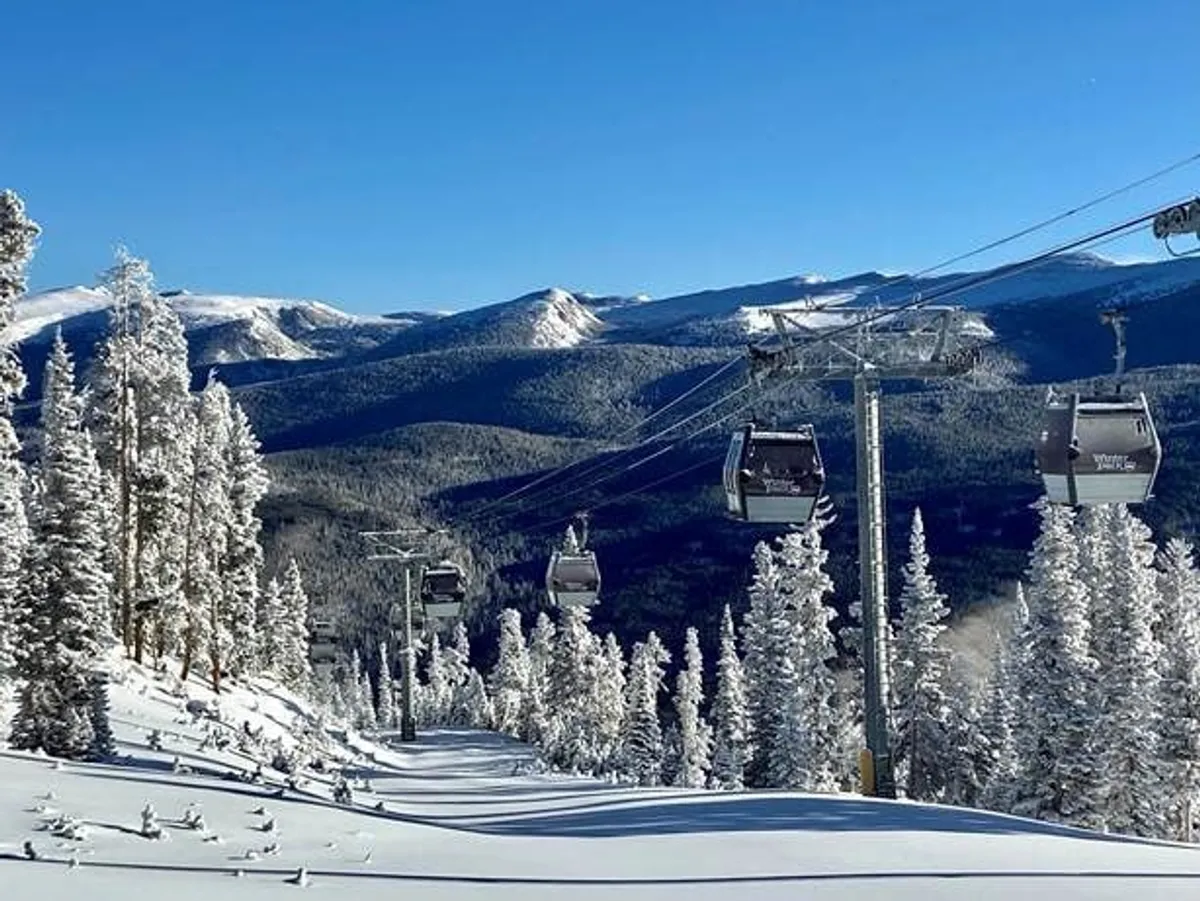 This exterior shot features a ski lift gliding over snow-covered trees with rugged mountains in the distance, conveying the thrill of alpine adventure and access to renowned ski terrain.