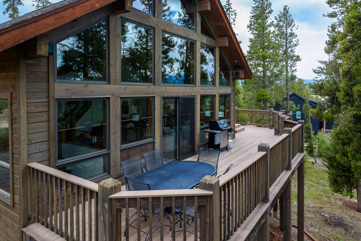 This image features a spacious deck with outdoor dining furniture and a grill, overlooking scenic mountain views and surrounded by nature. The setting is perfect for al fresco meals, sunset watching, or socializing with family, reinforcing the lodge's appeal as a retreat for all ages.