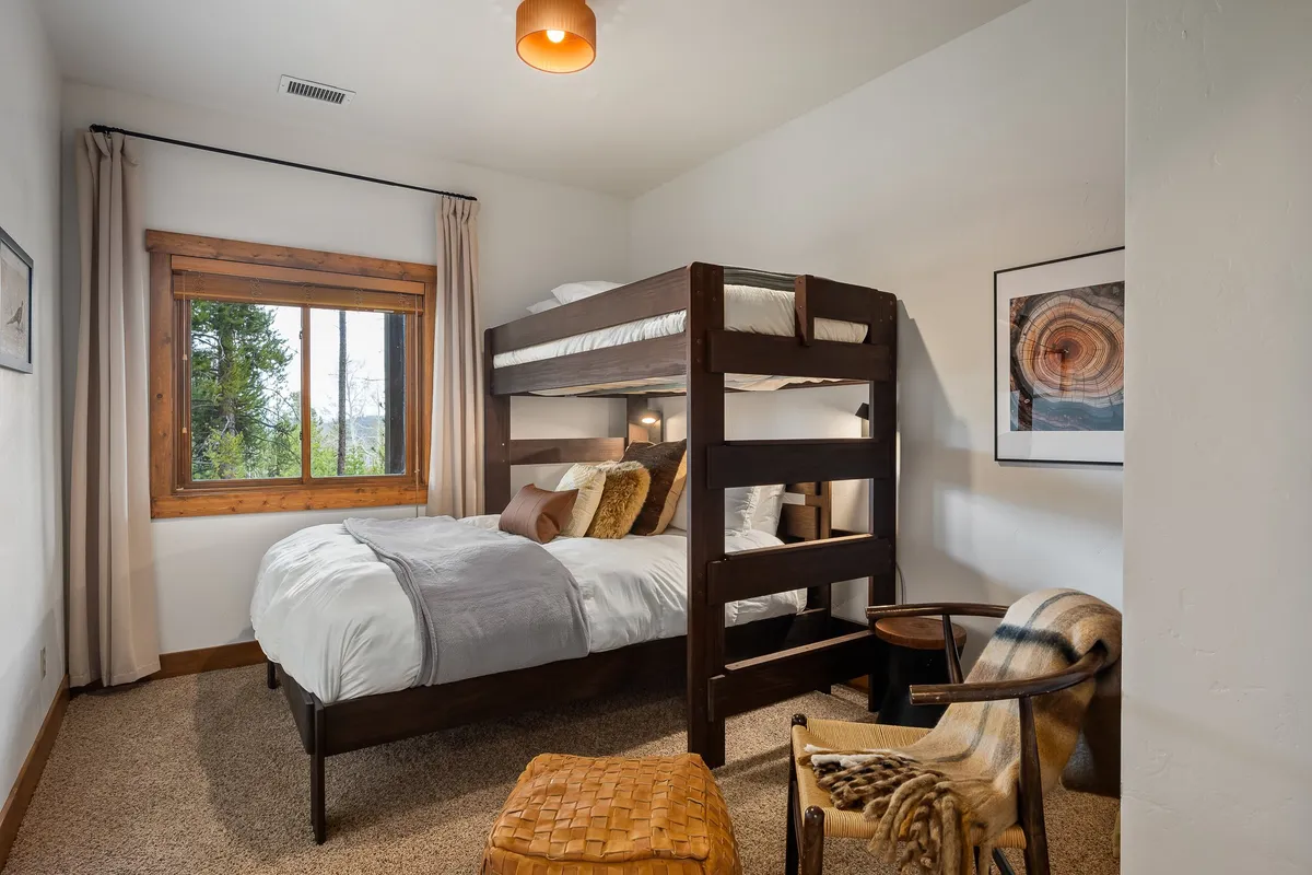 A bunk room featuring a sturdy bunk bed, an inviting armchair by the window, and natural light pouring in. The space is designed to be kid-friendly and flexible, perfect for families or extra guests, with cozy touches for comfort and play.