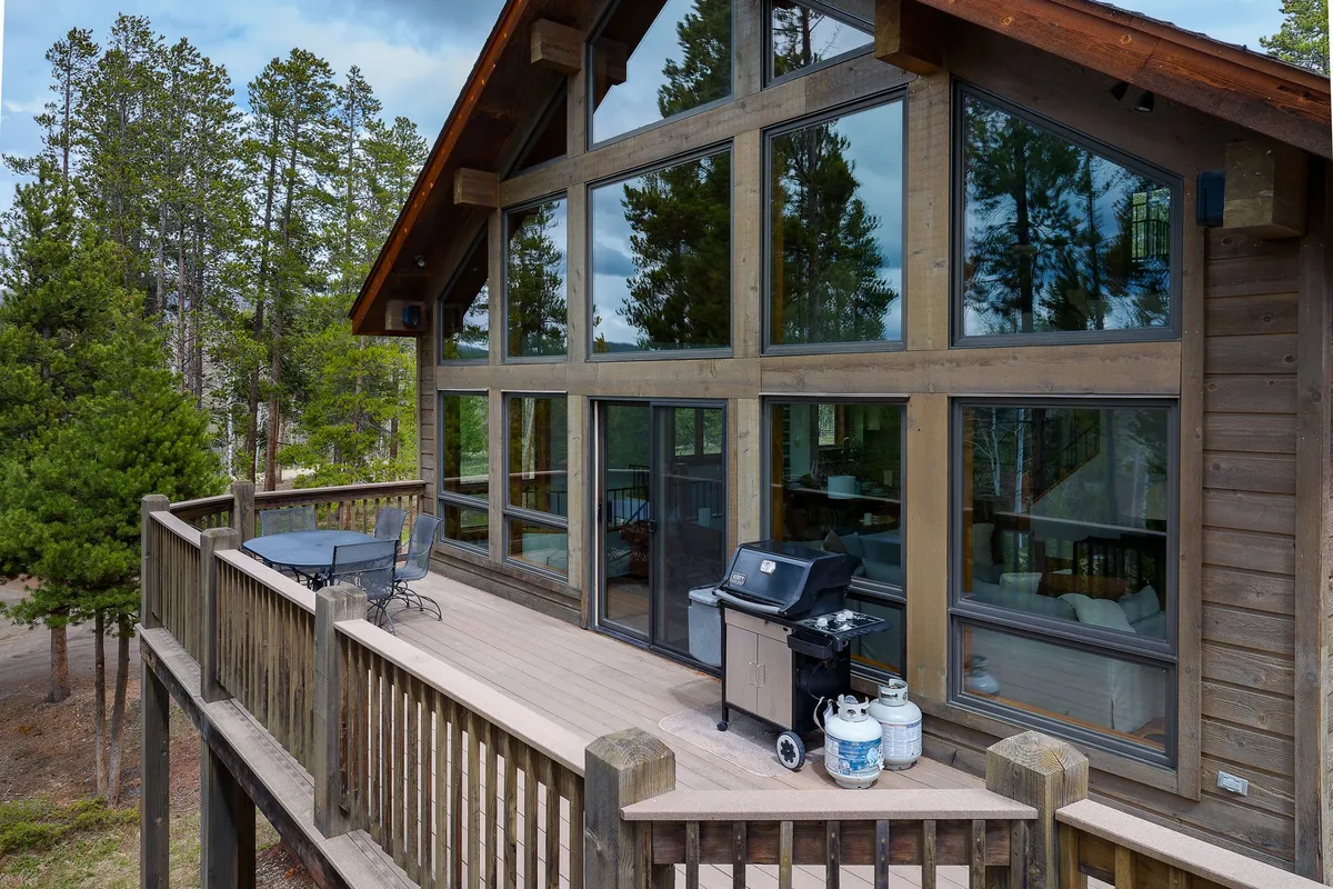 This exterior image features the lodge’s spacious deck area with large windows, a grill, and comfortable seating. Surrounded by natural beauty, the space is ideal for outdoor dining, relaxing, and enjoying panoramic views, creating a seamless connection between luxurious indoor amenities and the outdoors.