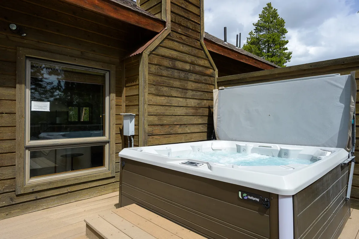 An inviting exterior scene of a private hot tub on a wooden deck, surrounded by tall trees. The setting is tranquil, evoking post-adventure relaxation and connection with nature, with the lodge’s deck blending seamlessly into its natural surroundings.