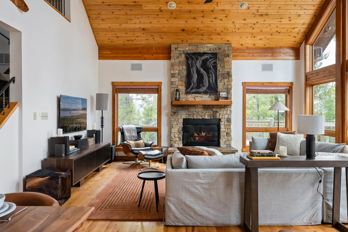 An intimate view of a cozy seating area with a stone fireplace, large windows, and comfortable chairs. The arrangement suggests an inviting space for socializing, playing board games, or simply unwinding while enjoying the natural scenery.