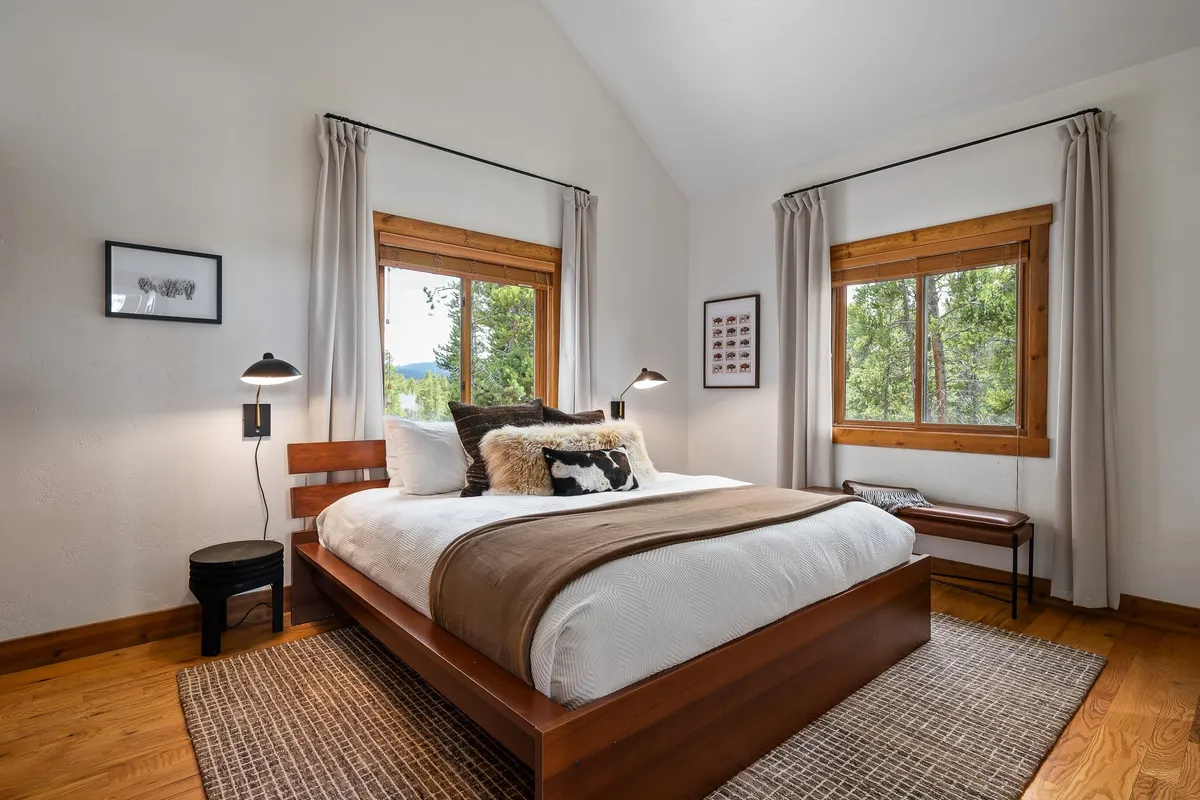 A serene bedroom with a comfortable bed positioned near large windows, allowing natural light to gently illuminate the space. Artwork adds a touch of personality, while the room's soft palette and layered textiles create a sense of calm, inviting relaxation and restful sleep.